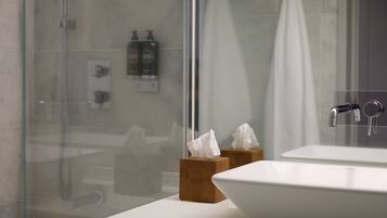 A bathroom with a glass shower enclosure, a white sink, and two wooden tissue boxes.
