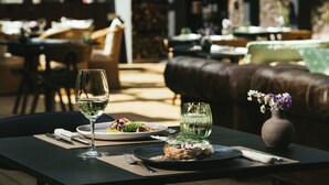 Una mesa de comedor con una copa de vino, platos de comida, un florero con flores y un cuchillo.