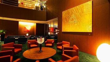 Un hall con una mesa redonda de madera, sillas anaranjadas, una estantería y una gran obra de arte iluminada en la pared.