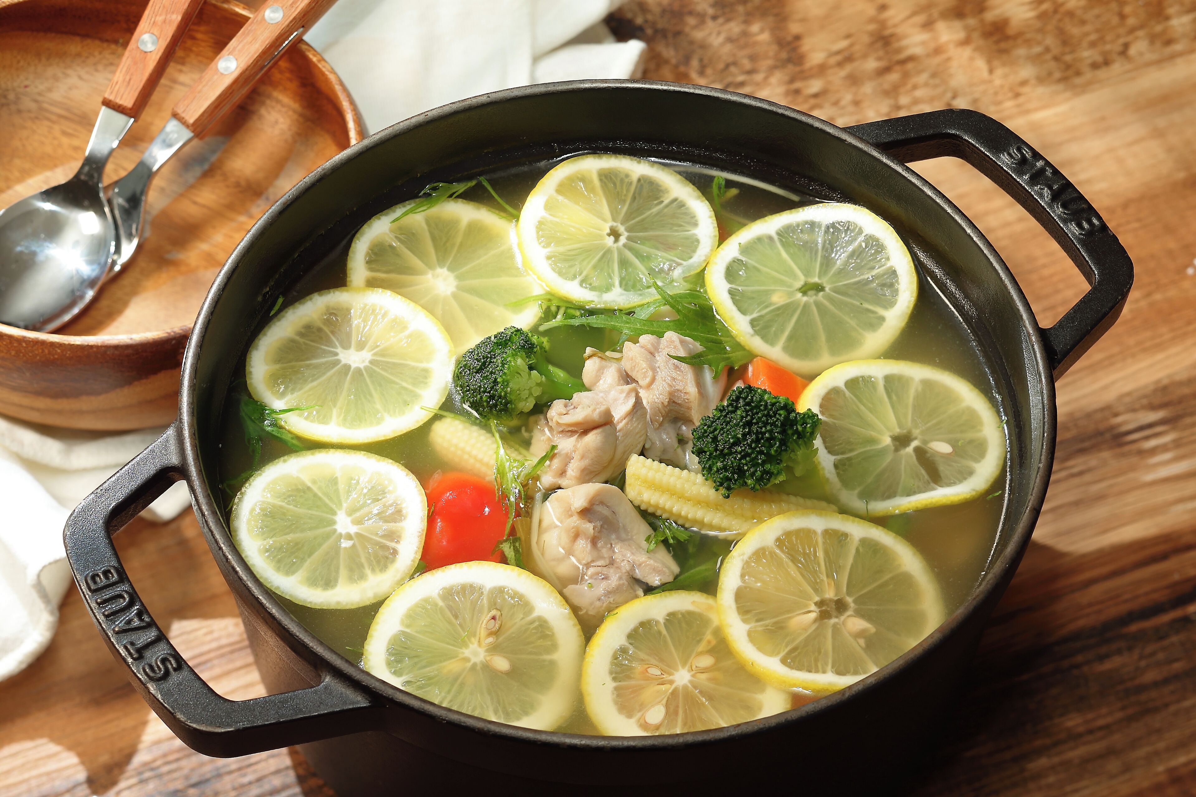 A pot of soup with lemon slices, chicken, broccoli, and carrots.