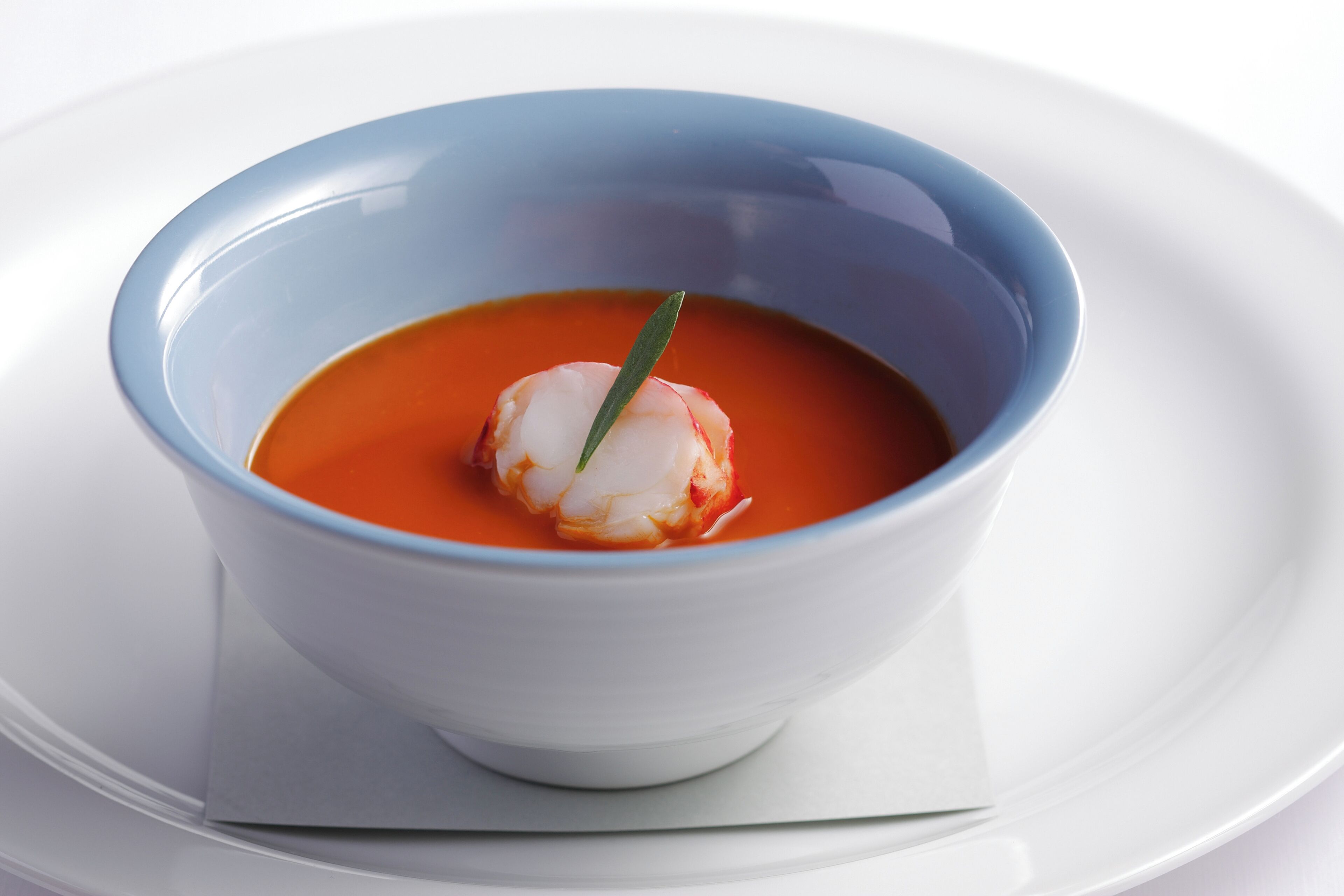 A bowl of soup with a garnish on a white plate.