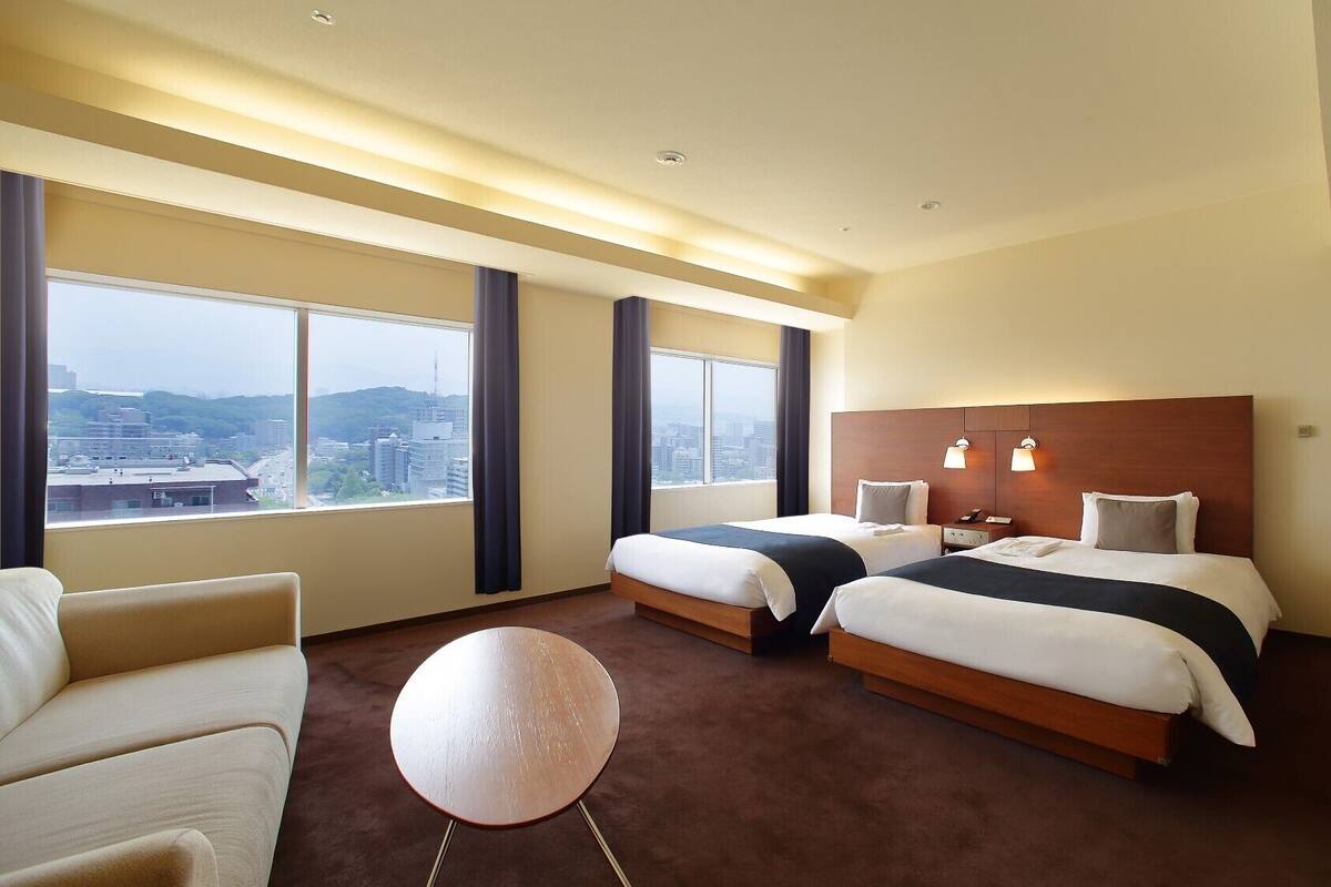 Habitación de hotel con dos camas, una mesa redonda y vistas a la ciudad.