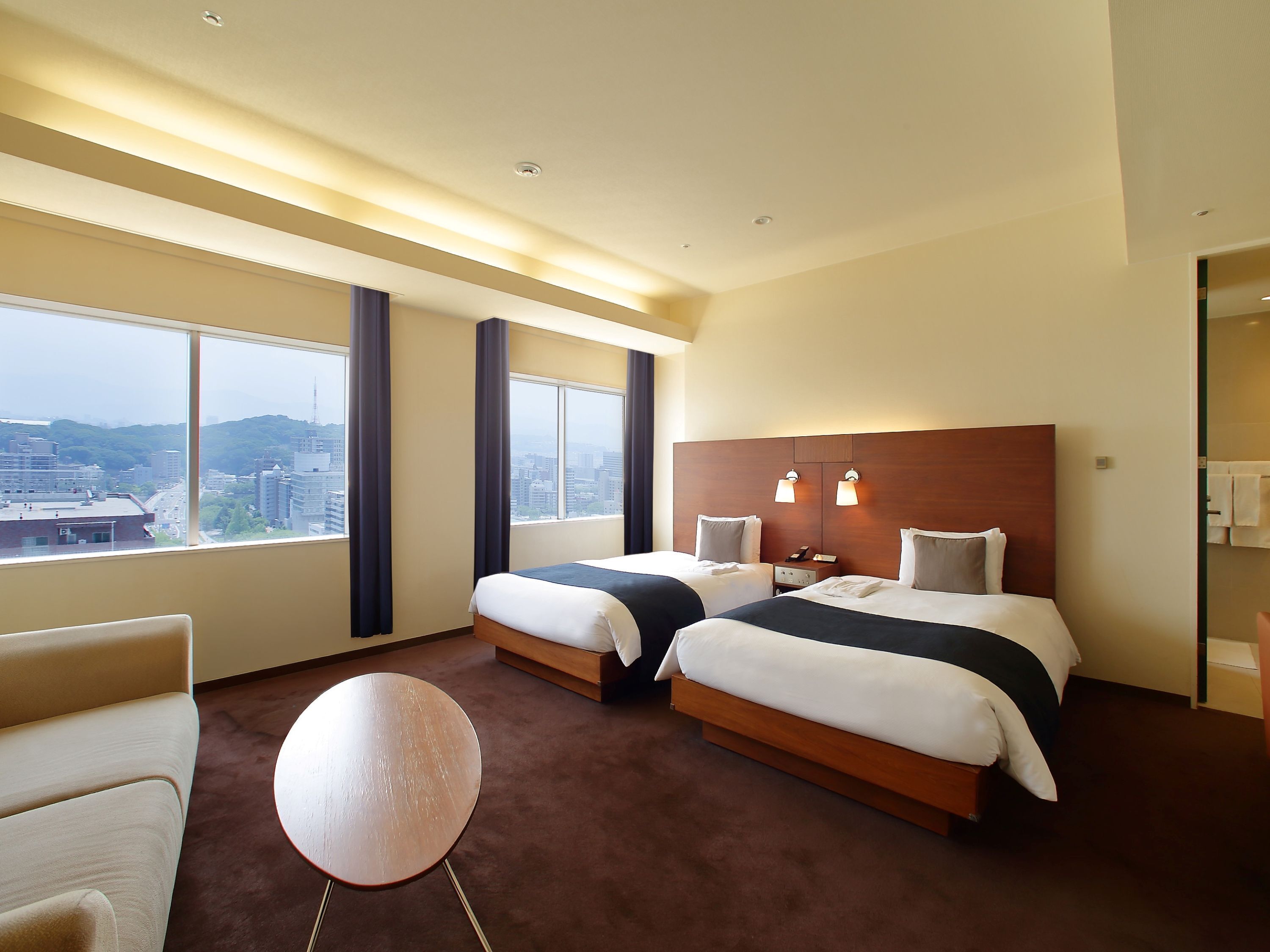 A hotel room with two beds, a round table, and a view of a cityscape.