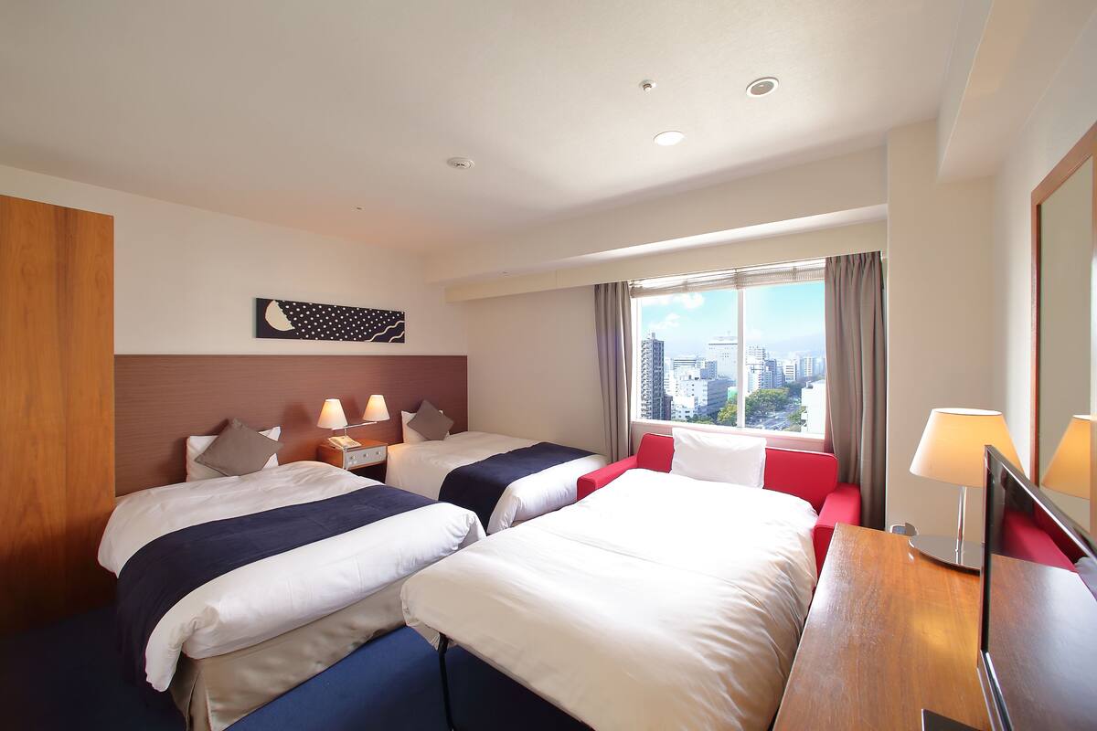 Habitación de hotel con dos camas, vista a la ciudad, cabecera de madera y escritorio con lámpara.