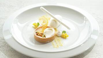 Une assiette blanche contenant un dessert composé d’une pâtisserie ronde, d’une boule de glace et d’un bâtonnet blanc, le tout décoré de fleurs jaunes et de tranches d’orange.