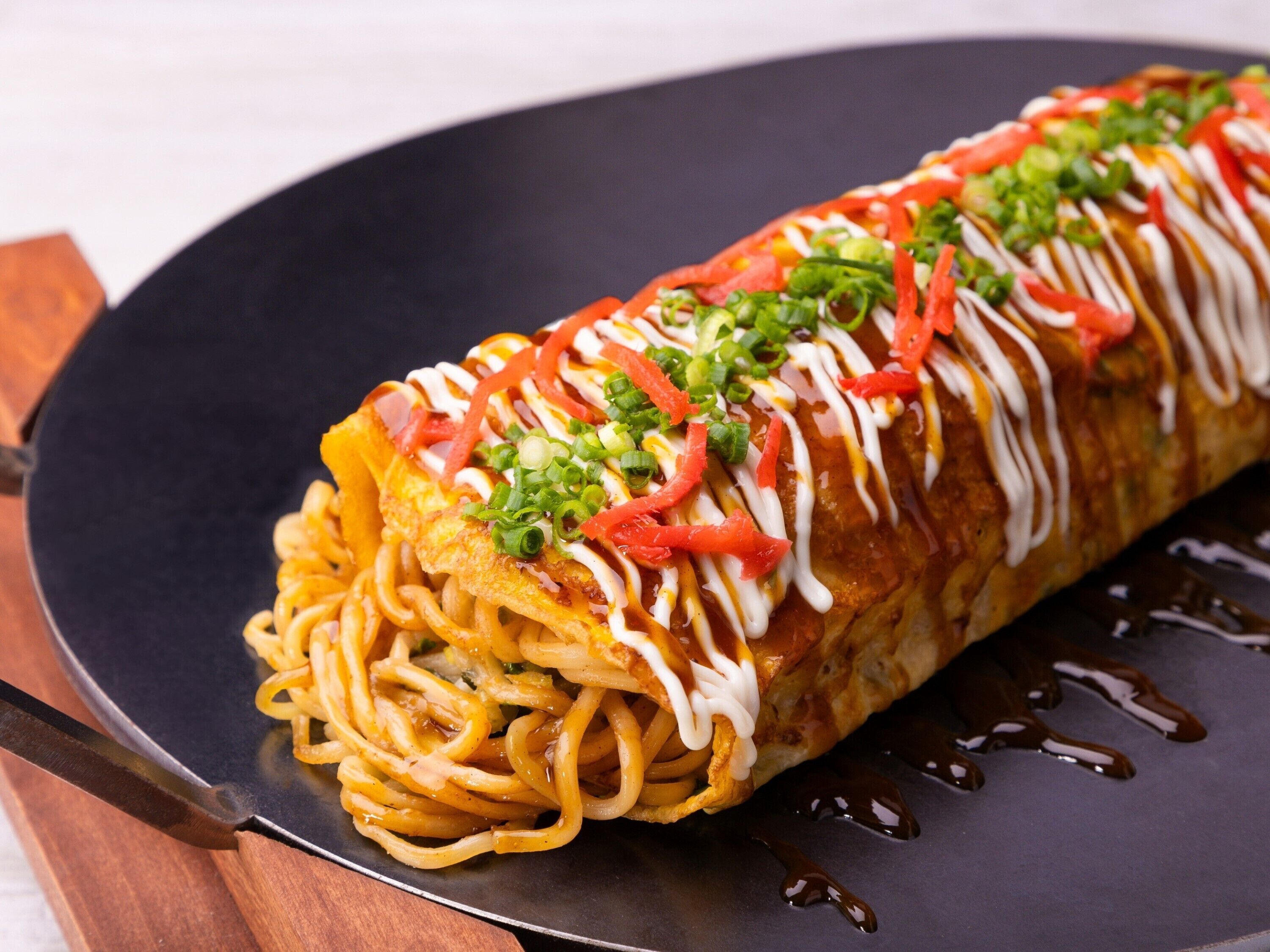 A dish with noodles, vegetables, and sauce on a black plate.