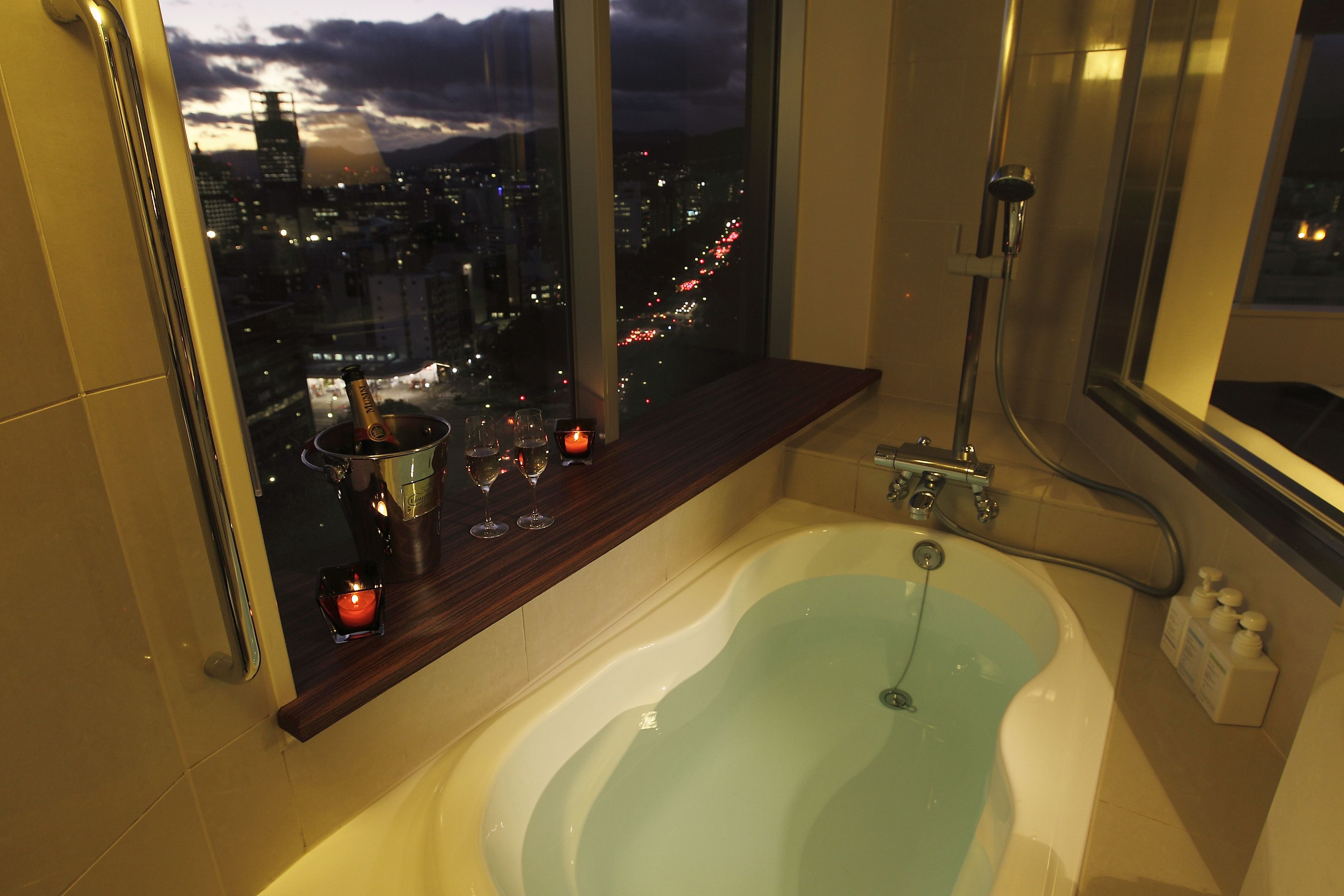 A bathtub with a view of a cityscape at dusk.