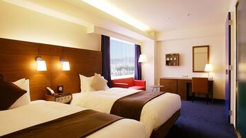 A hotel room with two beds, a desk, a chair, a mirror, and a view of the city.