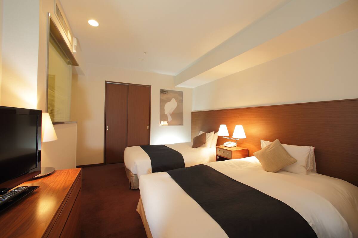 Una habitación de hotel con dos camas, televisión y un escritorio con lámpara.