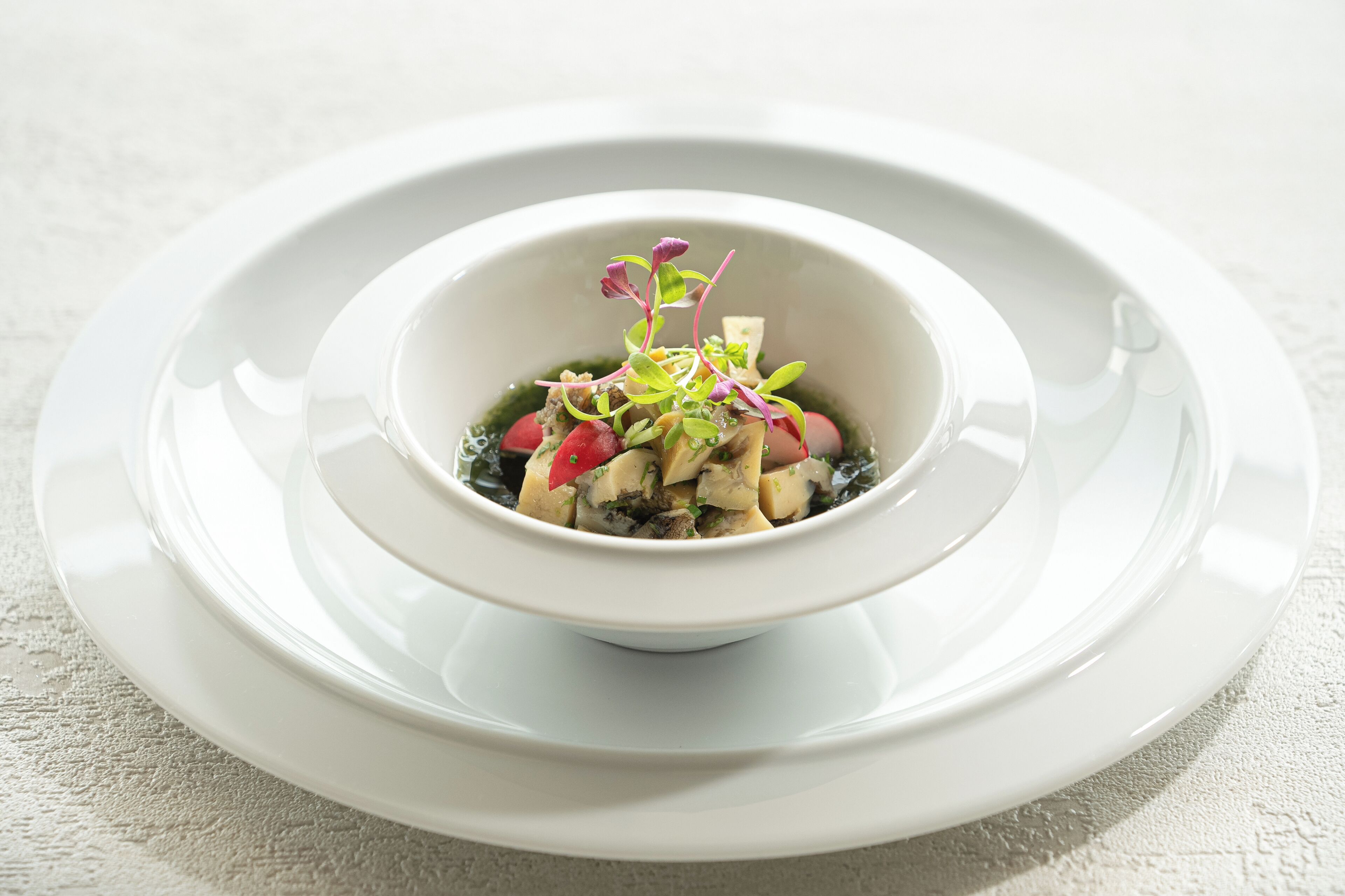 A white bowl of food with a decorative garnish on a white plate, placed on a textured surface.