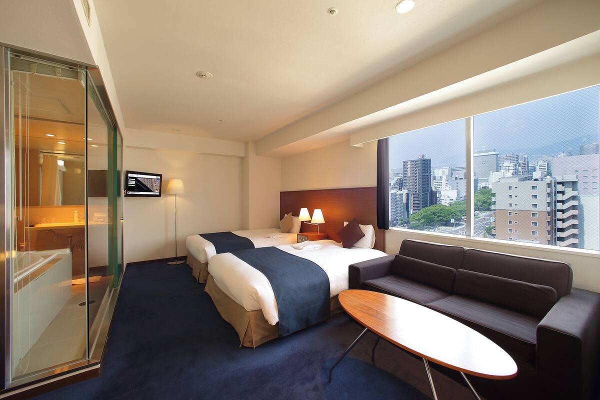 Habitación de hotel con dos camas, un sofá, una mesa, un televisor y vistas a la ciudad.