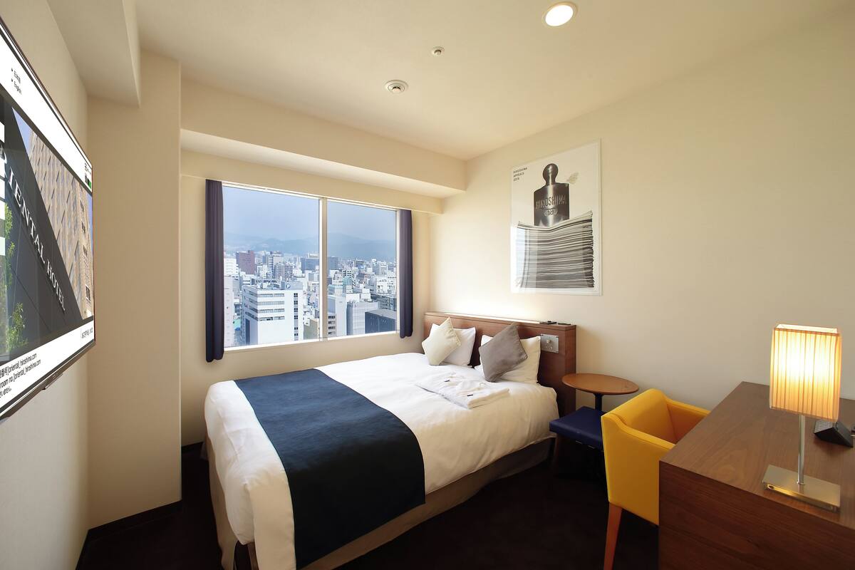 Habitación de hotel con una cama grande, un escritorio, una silla y vistas a la ciudad.