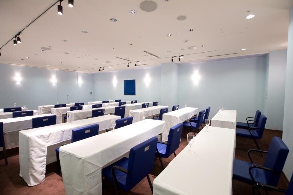 Un salón de conferencias con varias mesas y sillas, manteles blancos y sillas azules.