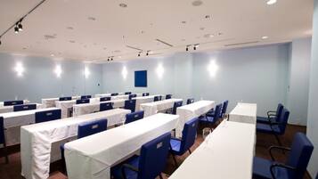 Un salón de conferencias con varias mesas y sillas, manteles blancos y sillas azules.