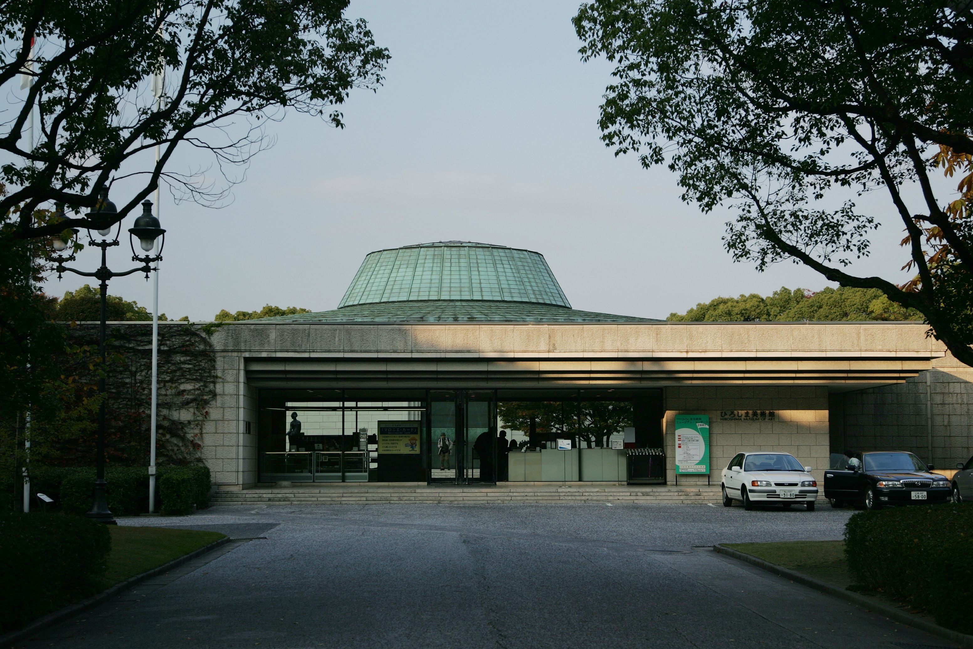 Un edificio con techo de cúpula verde, vestíbulo cubierto y zona de estacionamiento con automóviles.