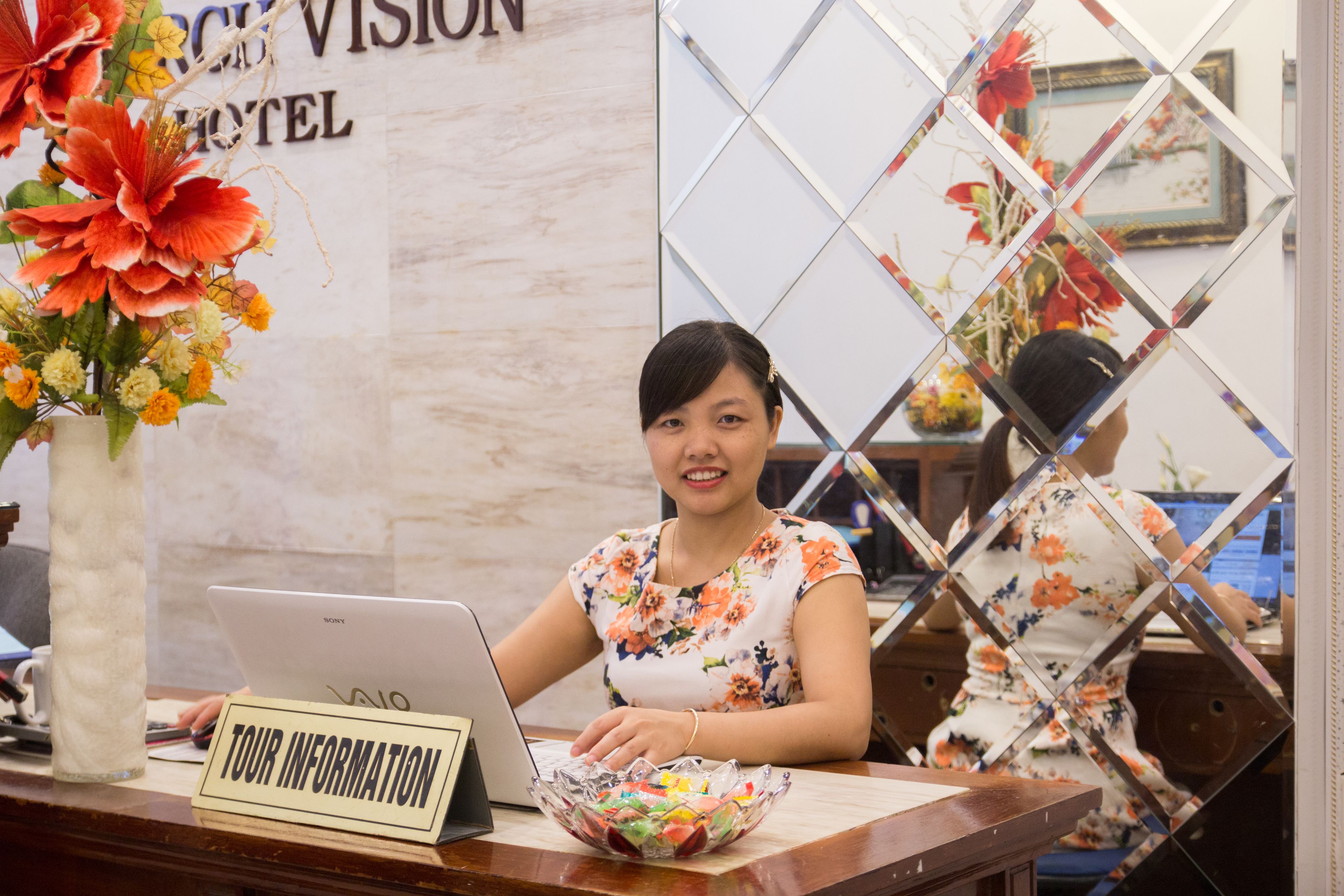 A reception desk with a laptop, a sign reading "TOUR INFORMATION", and a floral arrangement.