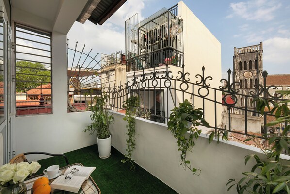 A balcony with a white railing, potted plants, a table with a book, a cup, and oranges.