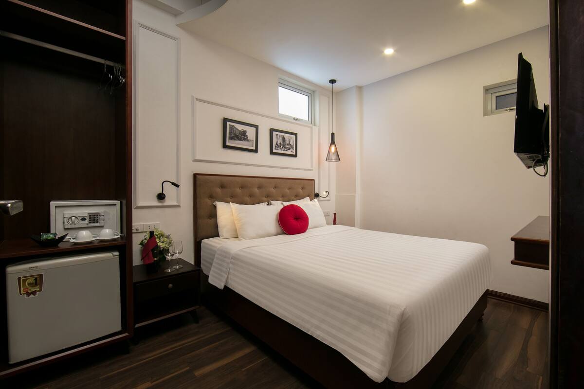 A hotel room with a large bed, a small kitchenette, a television, and a window.