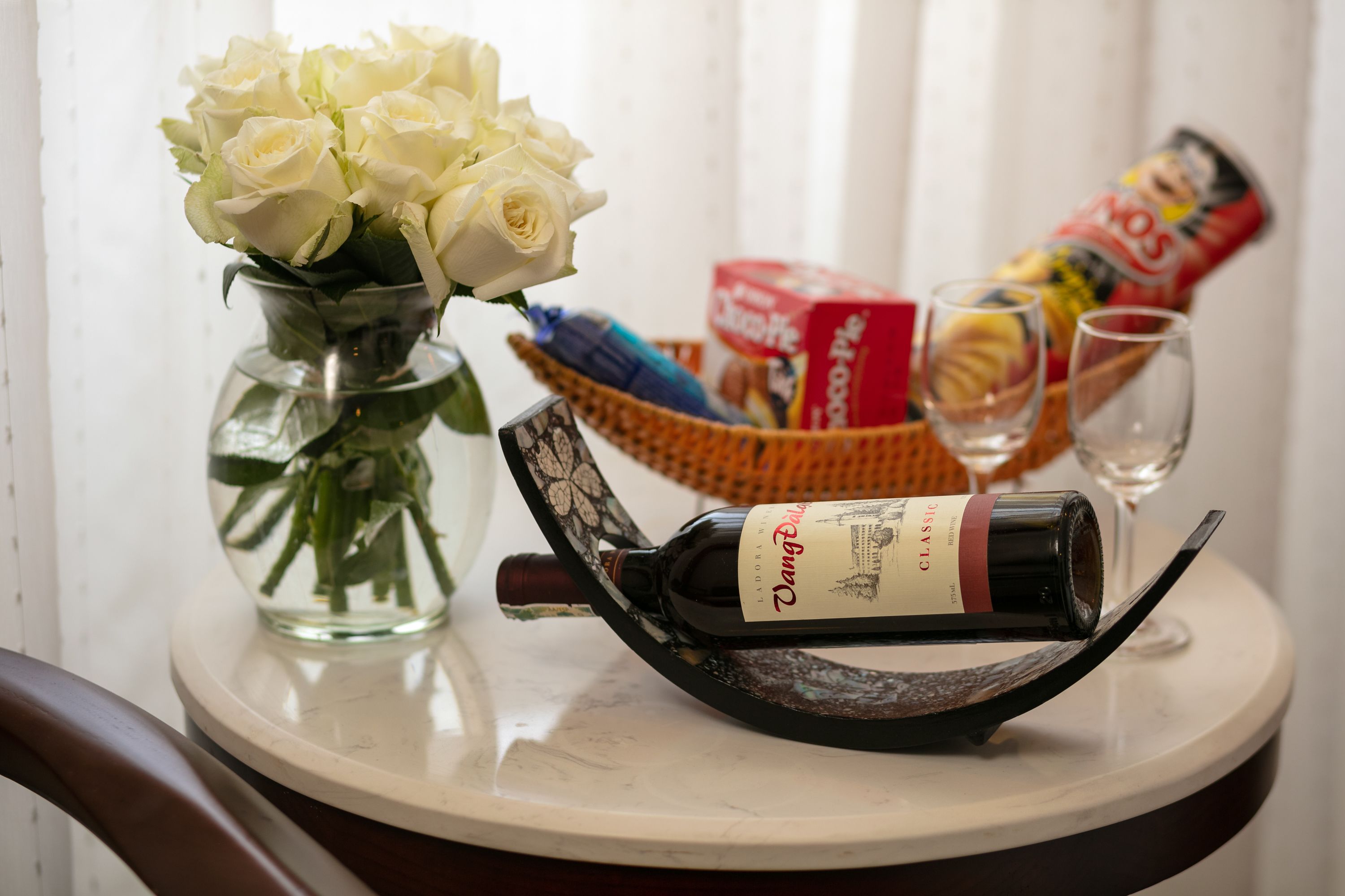 Ein Tisch mit einer Weinflasche, einer Rosenvase, einer Snackkörbchen und zwei Gläsern.