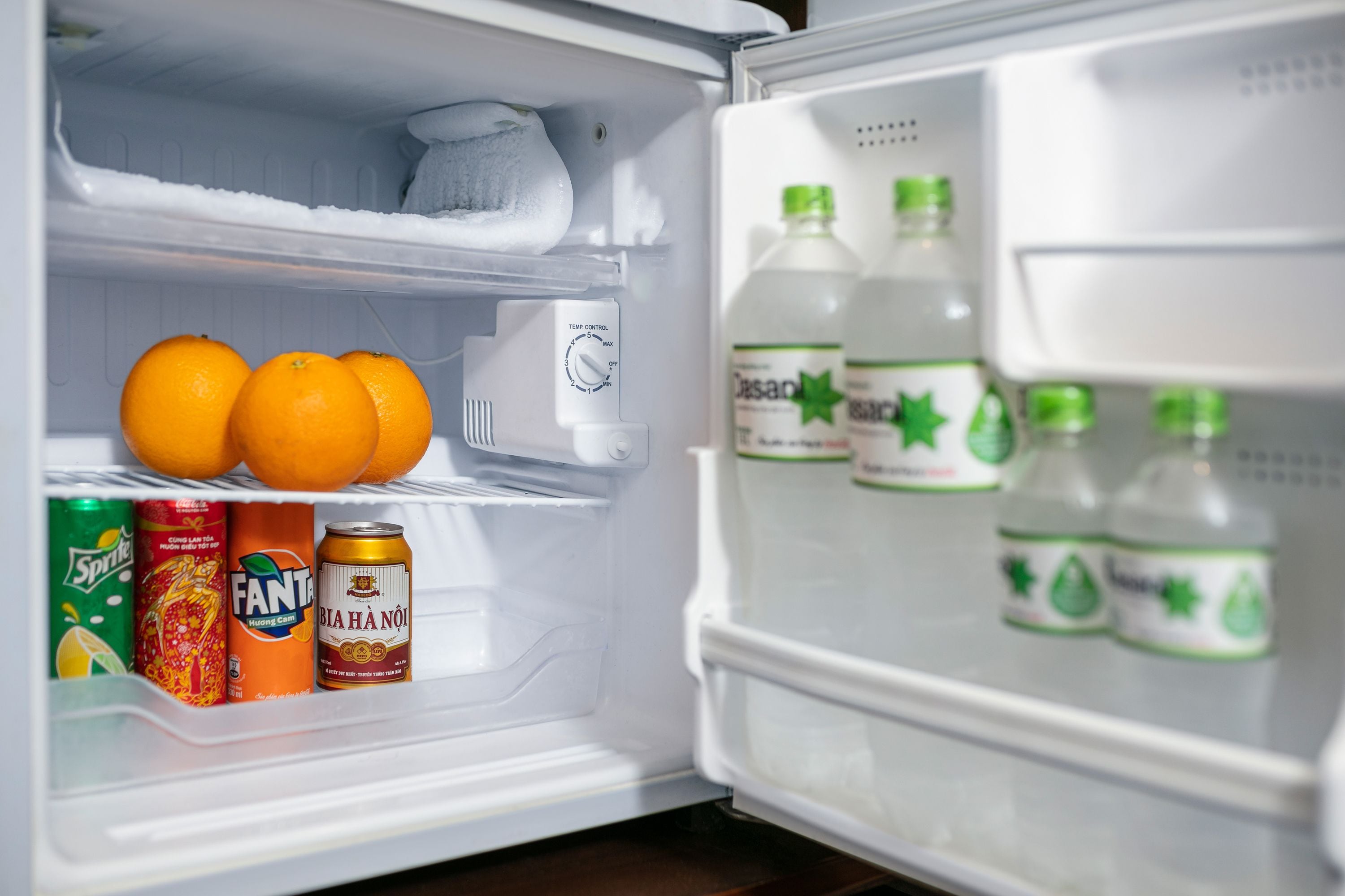 Un réfrigérateur contenant des oranges, des canettes de soda et des bouteilles d’eau.