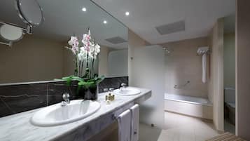 A modern bathroom with two sinks, a large mirror, a shower, and a small bench.