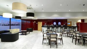 A modern hotel lobby with a bar area, seating arrangements, and a view of the cityscape.