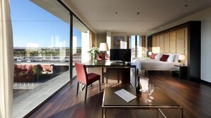 Ein modernes Hotelzimmer mit großem Fenster, Schreibtisch mit Stuhl, Bett und Fernseher.