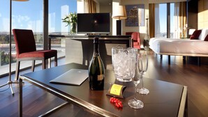 Ein Hotelzimmer mit einem großen Fernseher, einem Bett, einem Schreibtisch mit einem Laptop, einer Weinflasche und einem Eimer Eis.