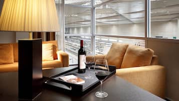 Una habitación de hotel moderna con un ventanal grande, un sofá, una mesa con una bandeja que contiene una botella de vino, una copa y un menú.