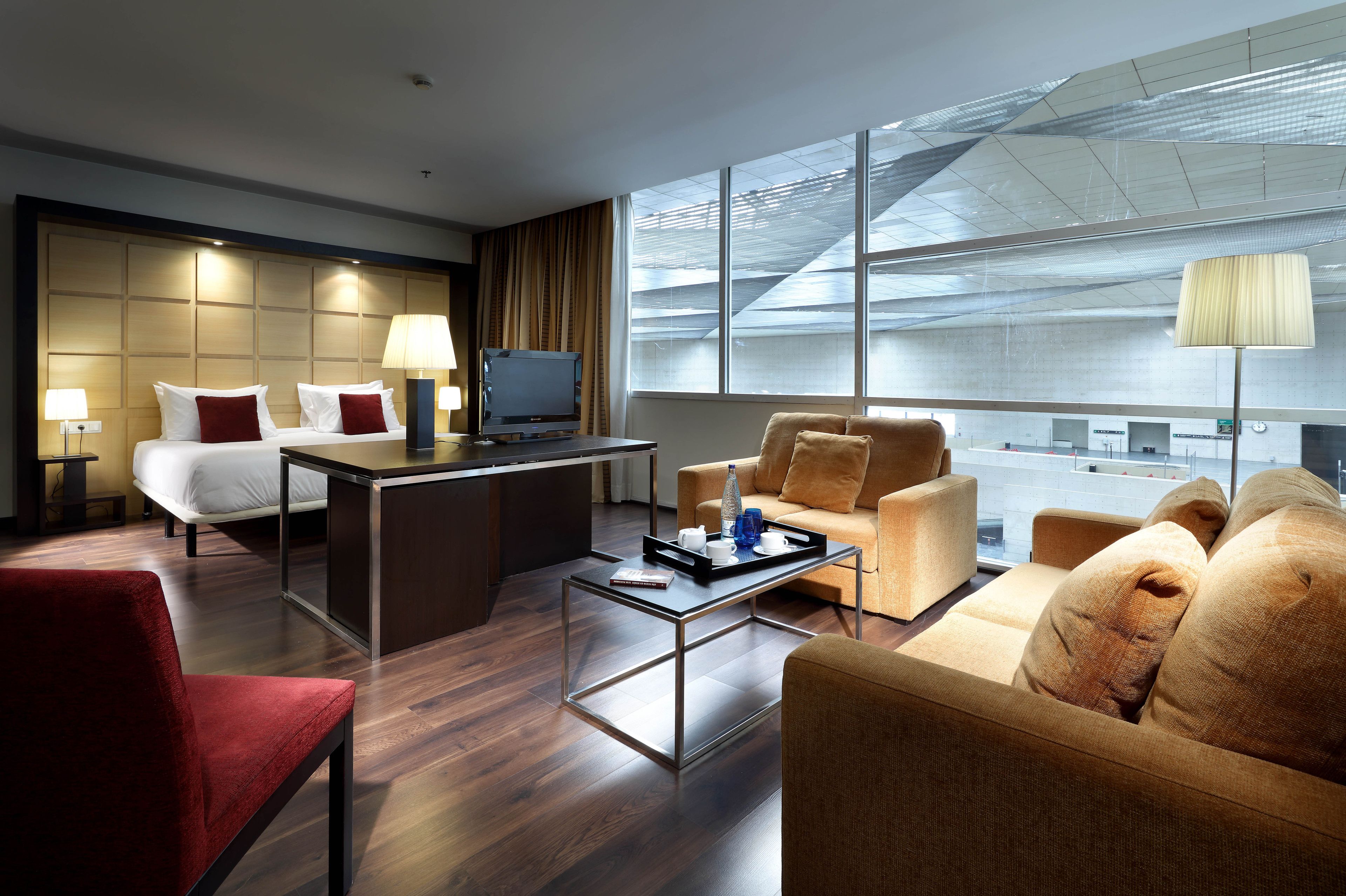 Habitación de hotel con cama, escritorio, sofá y un amplio ventanal con vistas a la ciudad.
