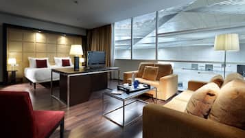 A hotel room with a bed, a desk, a sofa, and a large window with a view of the city.