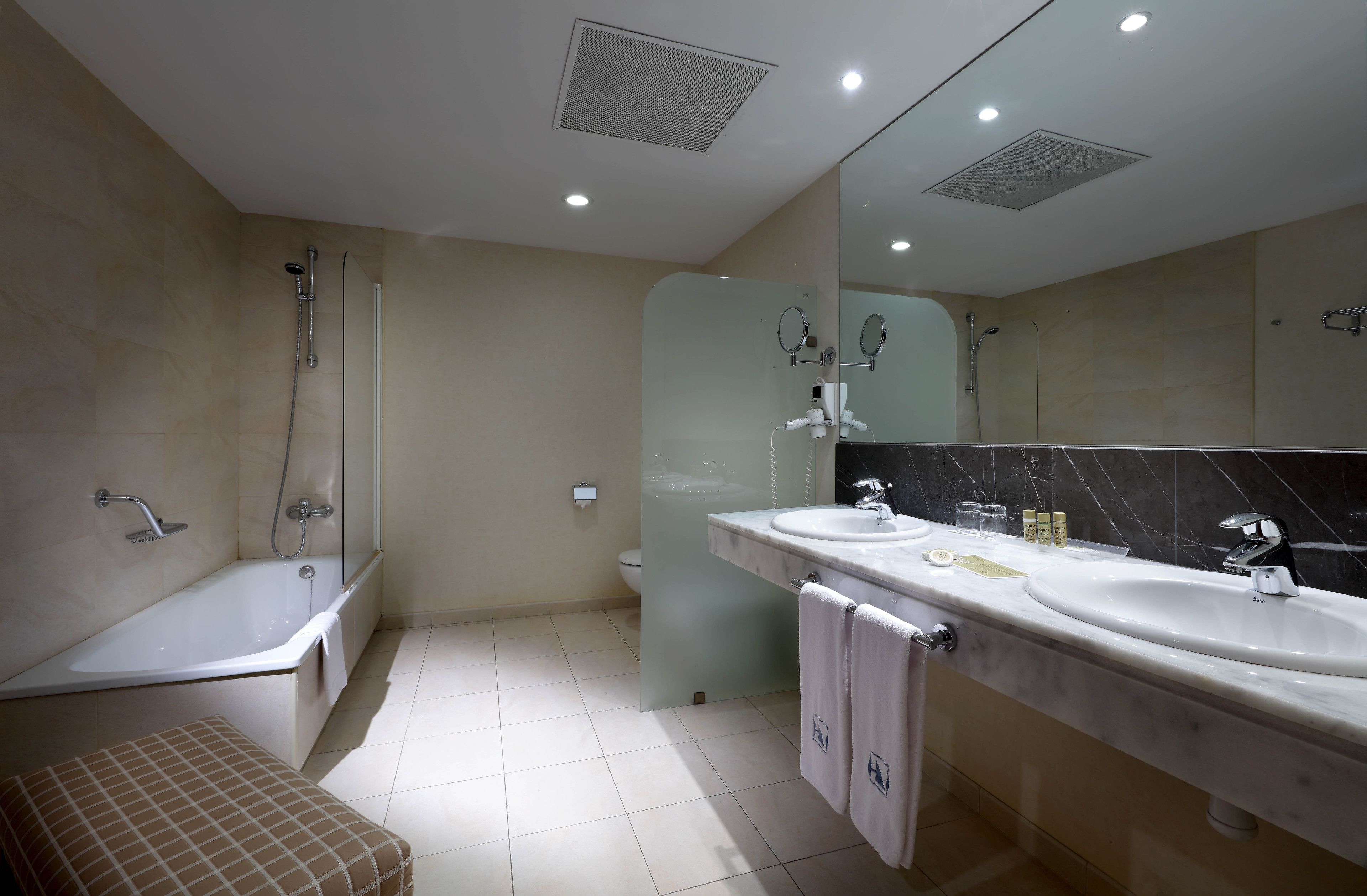Un baño moderno con bañera, dos lavamanos, un espejo grande y una ducha con cerramiento de vidrio.