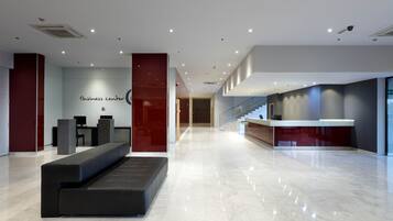 A modern business center with a reception desk, seating area, and a staircase leading to upper floors.