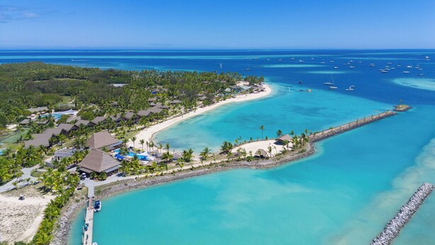 An aerial view of a coastal resort with a beach, clear turquoise waters, and a pier.