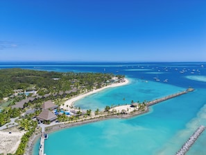 An aerial view of a coastal resort with a beach, clear turquoise waters, and a pier.