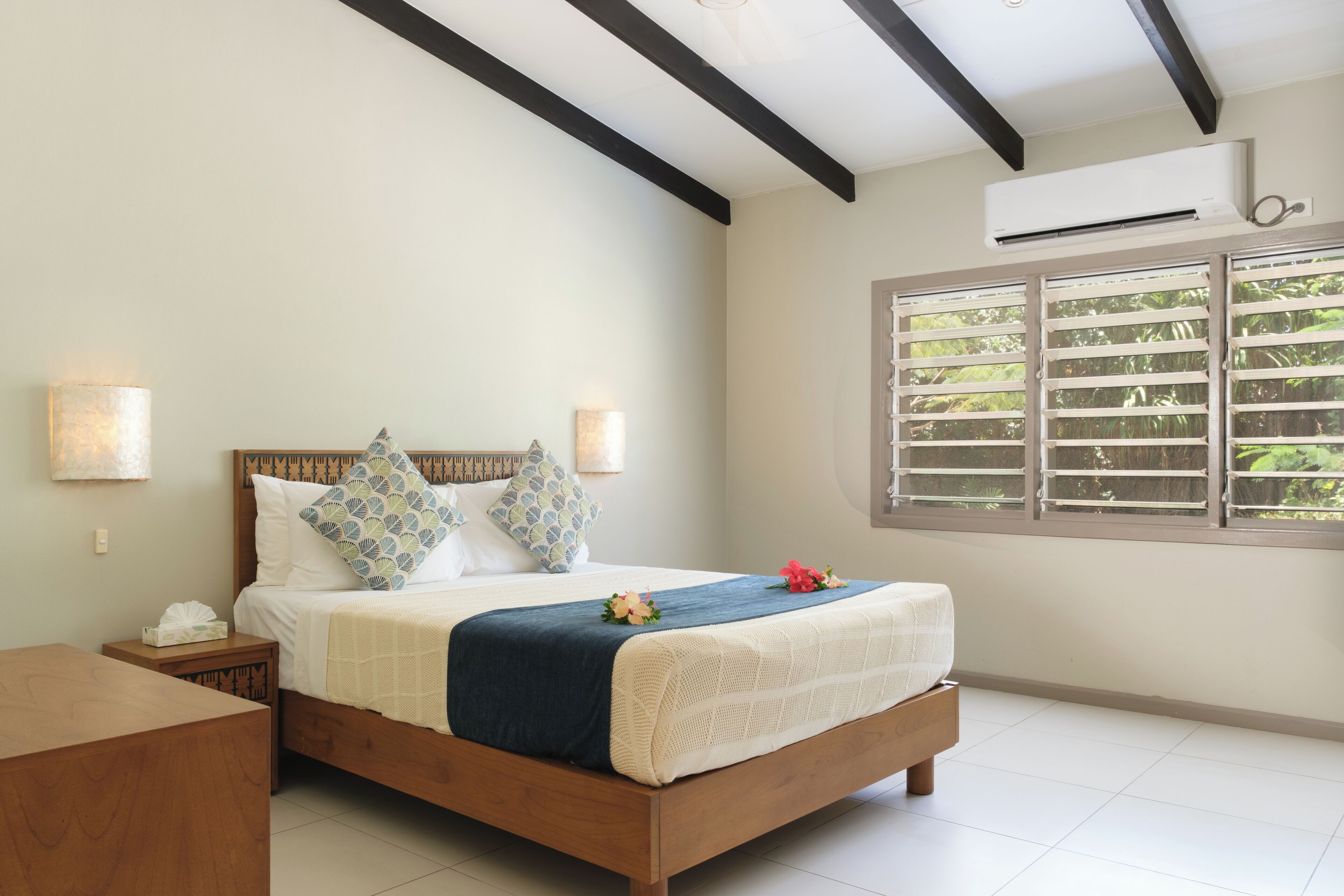 A bedroom with a wooden bed, white bedding, and a window with blinds.