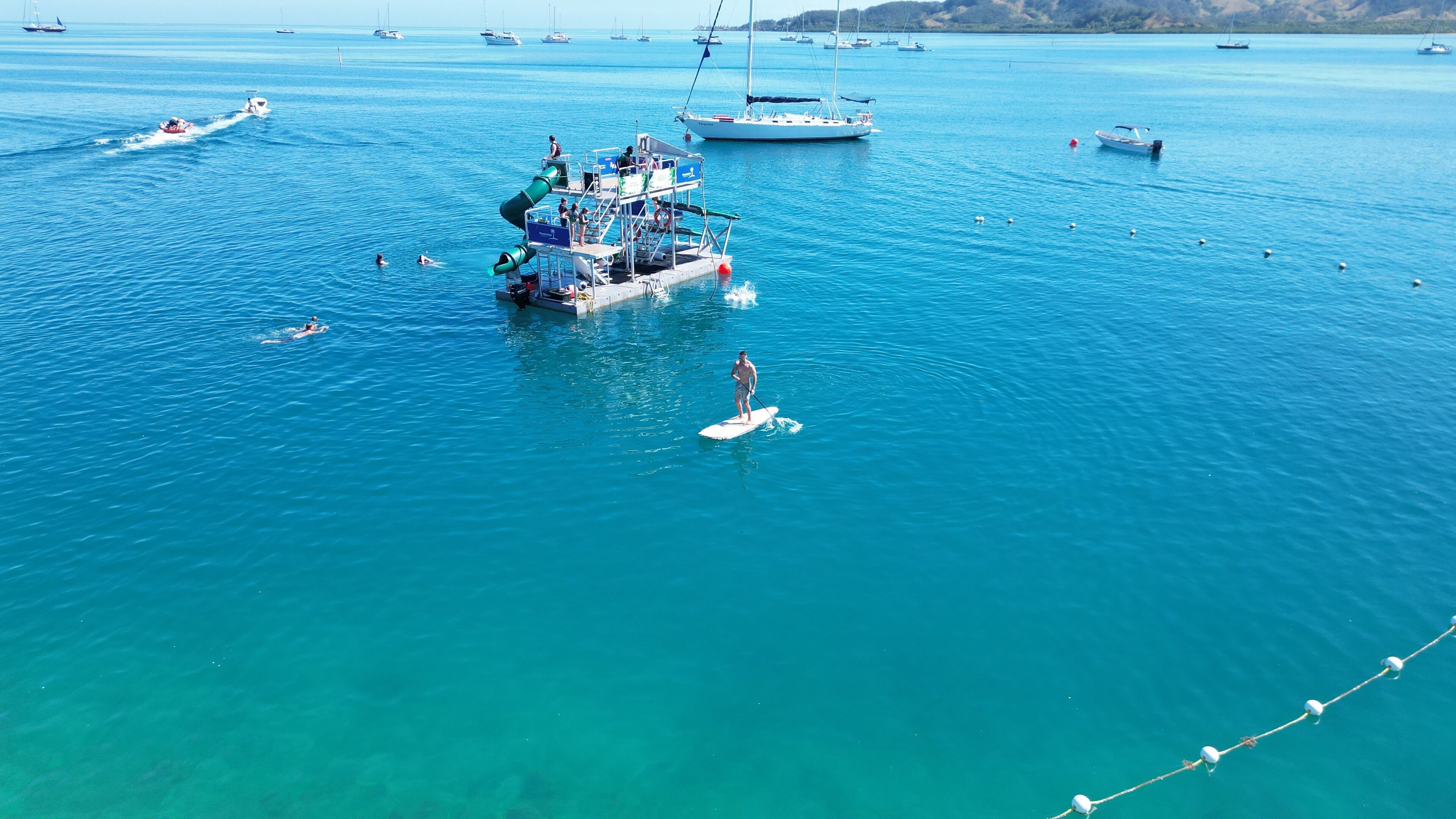 A pier with a boat docked, surrounded by calm blue waters and several boats in the distance.