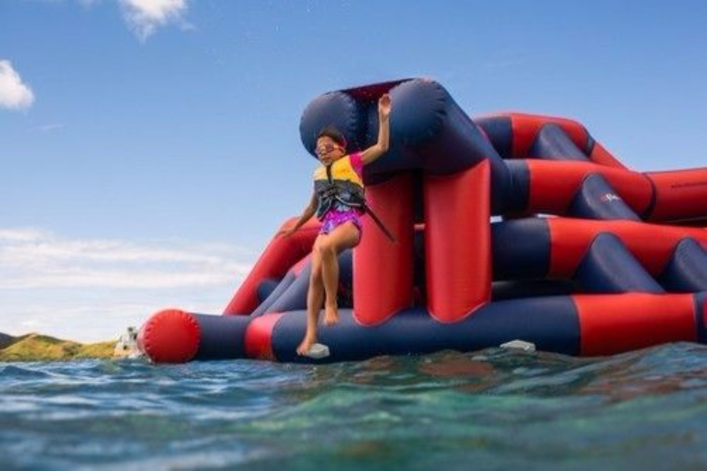 A person sitting on a large, multi-colored inflatable structure in the water.
