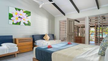 Une chambre avec deux lits, une commode en bois, un ventilateur de plafond et une grande fenêtre donnant sur une piscine.