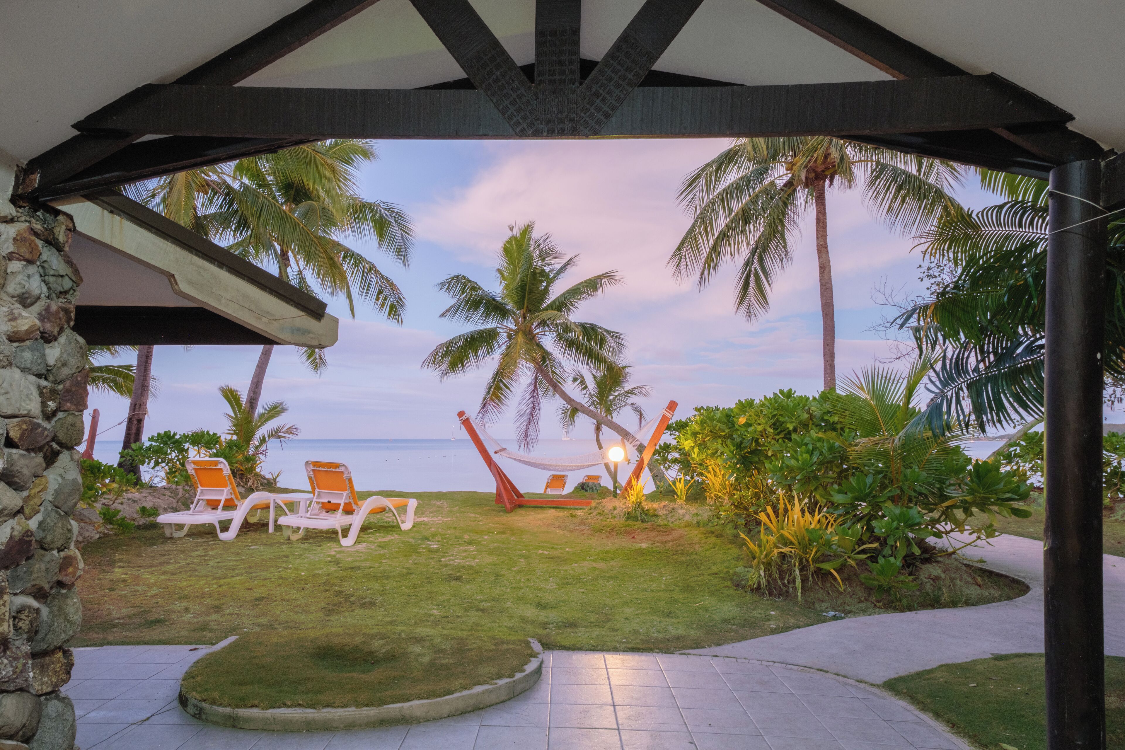 A covered outdoor area with a hammock, lounge chairs, and a view of the ocean.