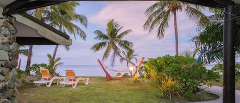 A covered outdoor area with a hammock, lounge chairs, and a view of the ocean.