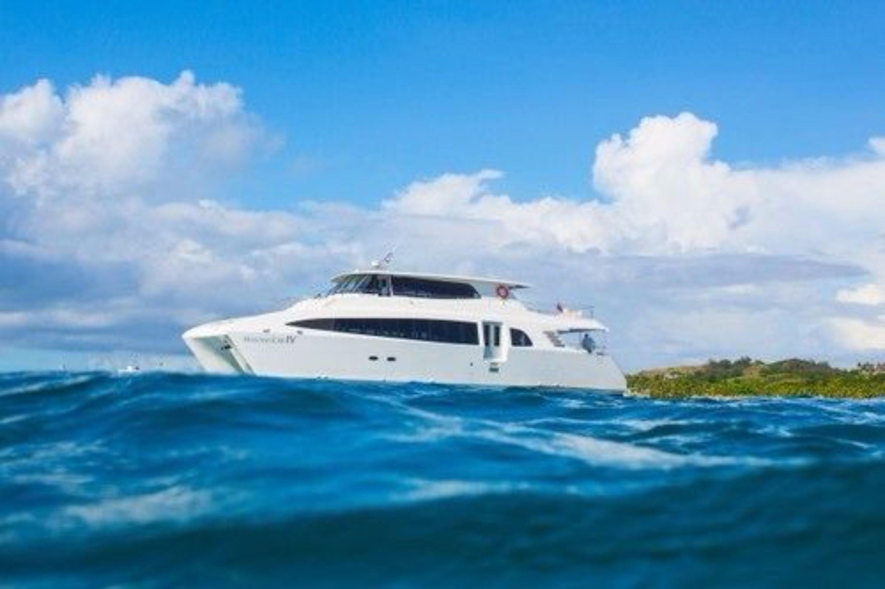 Un yate blanco en el agua, con cielo despejado y nubes al fondo.