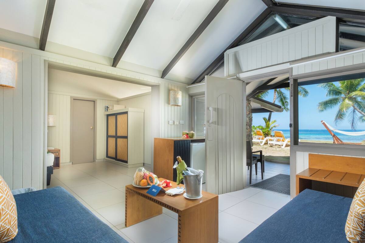 A room with a wooden table, a bed, and a view of the beach.