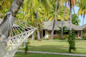 Un resort tropical con una hamaca, palmeras y un edificio de fachada de piedra.