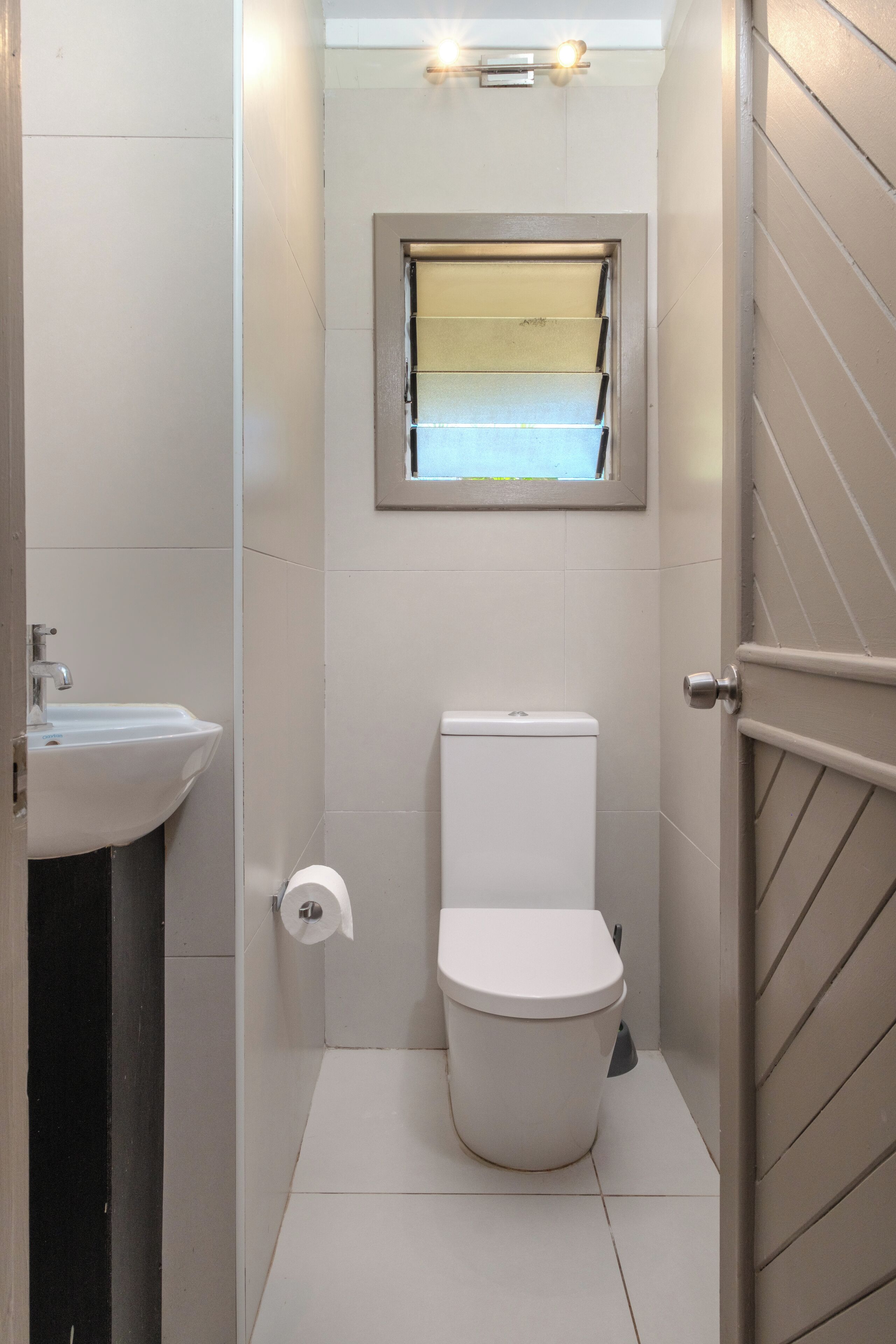 Un bagno piccolo e compatto con un water, un lavandino e una finestra sopra il water.