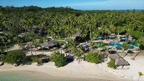 A resort with a swimming pool, beach, and palm trees.