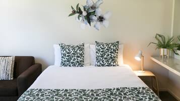 Een netjes ingerichte slaapkamer met een bed, kussens, een nachtkastje, een lamp en een wandplant.