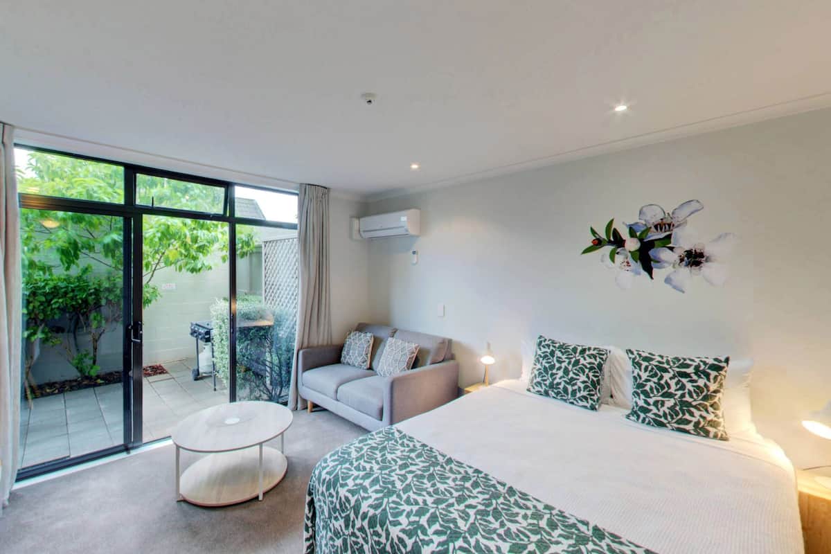 Habitación de hotel moderna con una cama grande, un sofá, un televisor y un balcón con vistas a zonas verdes.