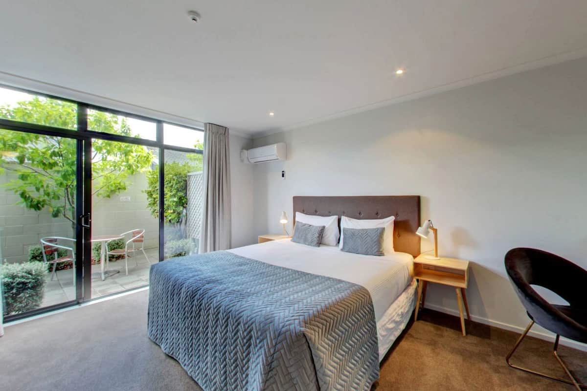 Una habitación de hotel moderna con una cama grande, un escritorio, una silla y un ventanal corredero que da a un balcón.
