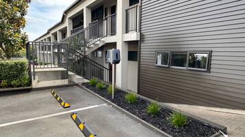 A modern building with a covered outdoor area, a staircase, and a parking lot with bollards.
